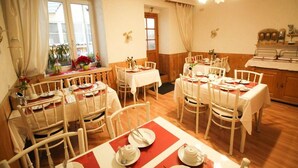 Un espace repas comprenant plusieurs tables et chaises, un lustre et une vue sur l’extérieur grâce à de grandes fenêtres.