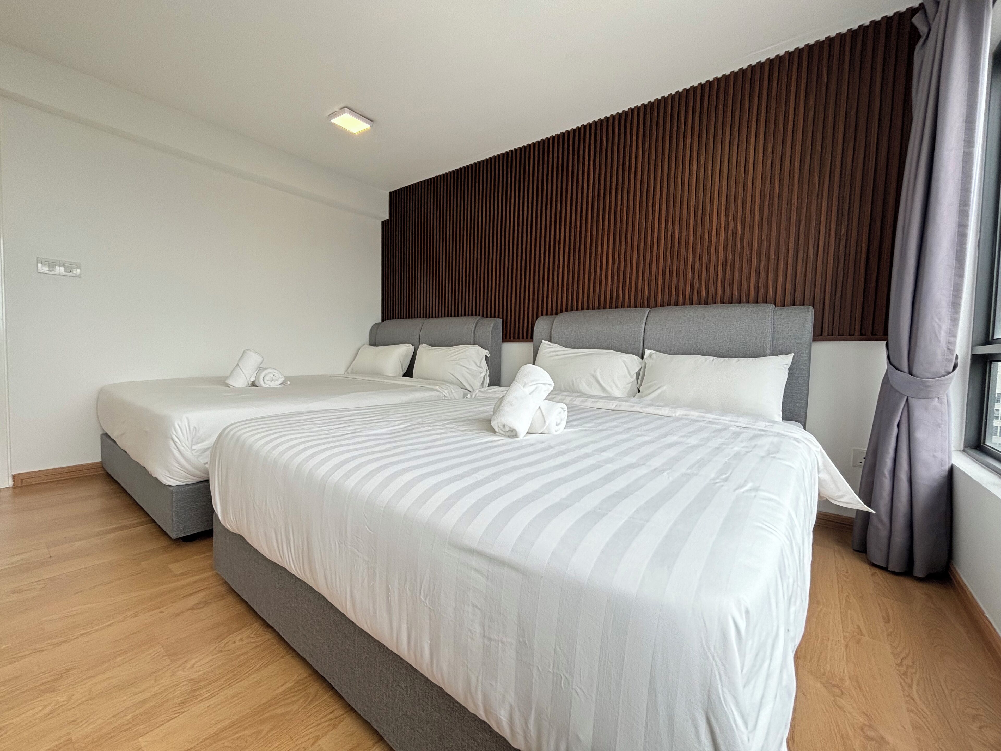 Habitación de hotel con dos camas, suelo de madera y un ventanal con cortinas.