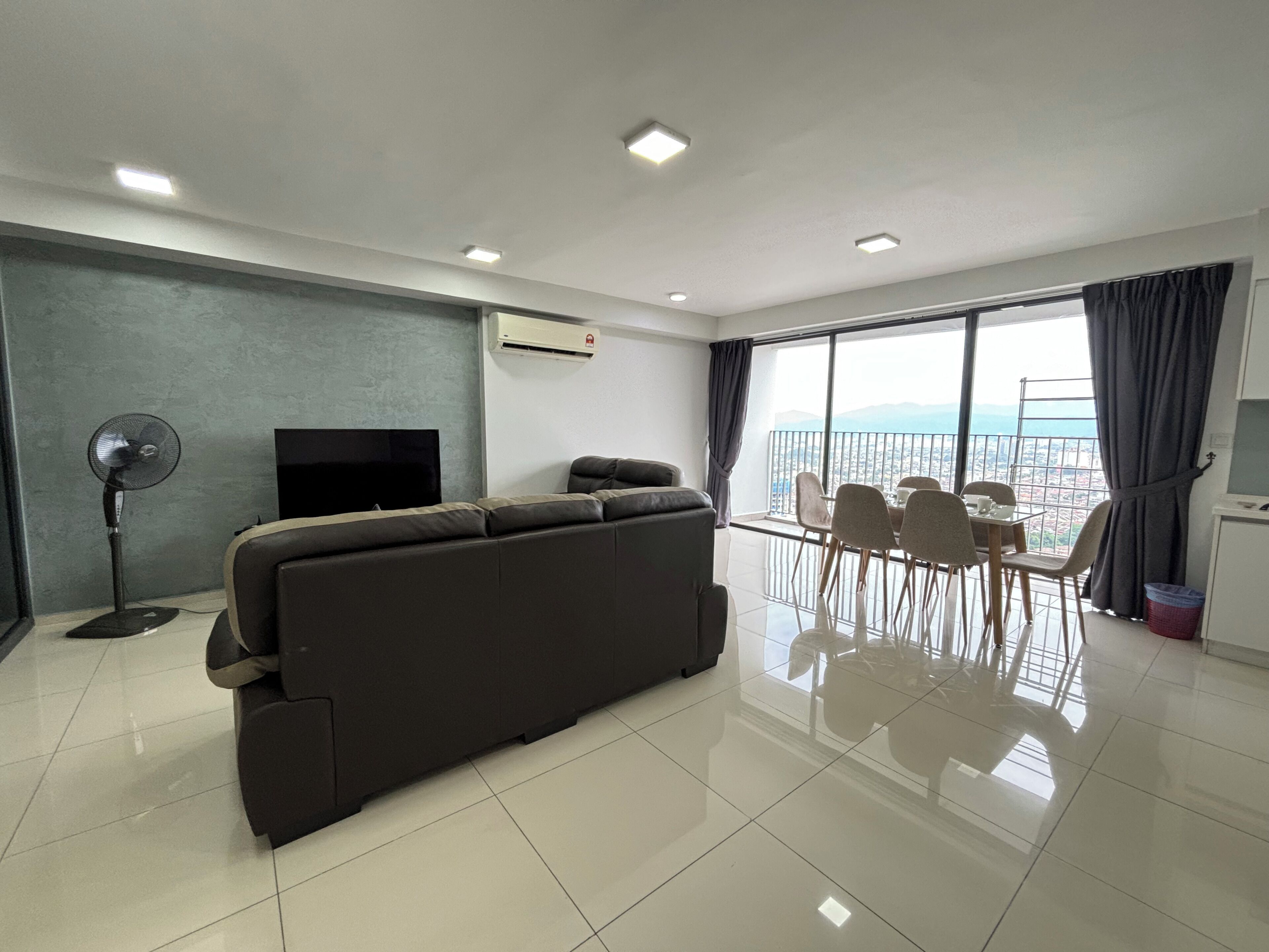 A modern living room with a sofa, TV, and balcony with dining area.