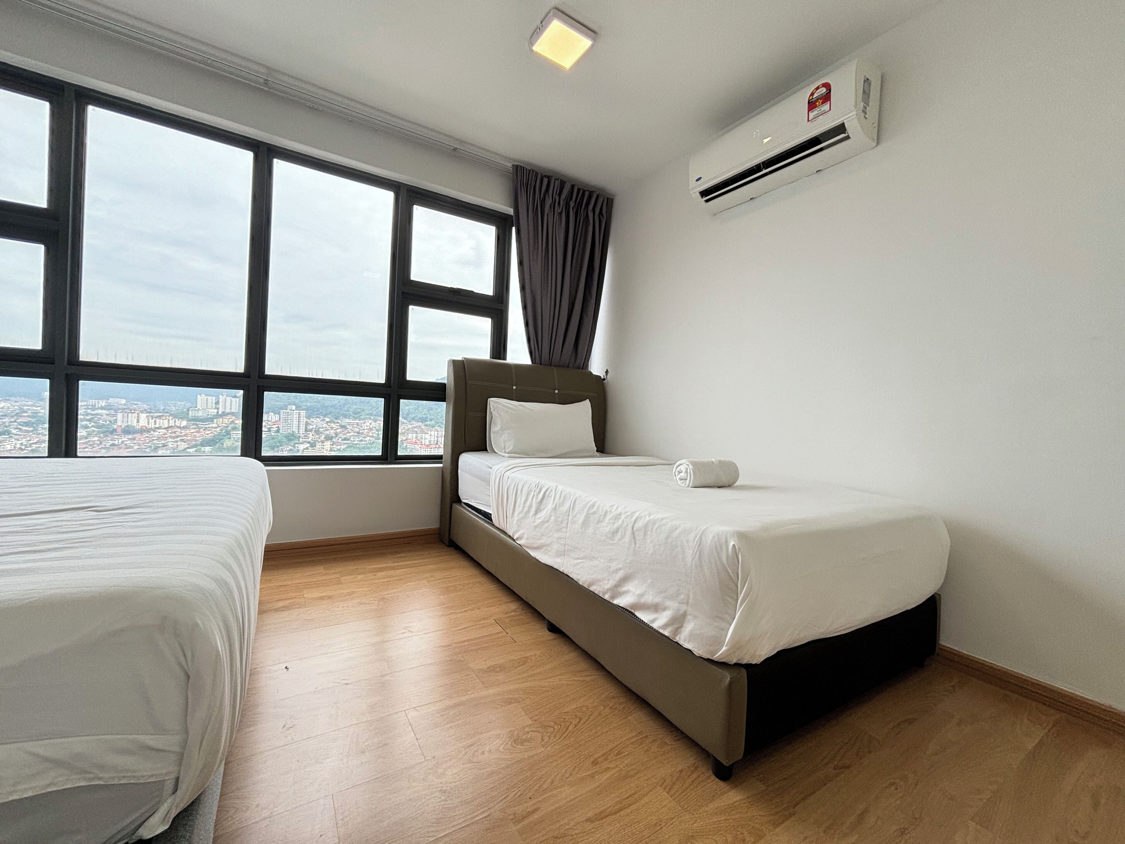 A hotel room with a bed, a window with a city view, and an air conditioning unit.