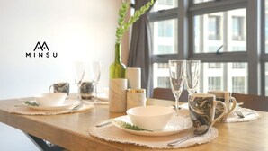 A dining table set with white bowls, silverware, and glassware, with a view of a building through a window. - Minsu Ekocheras (Kuala Lumpur)