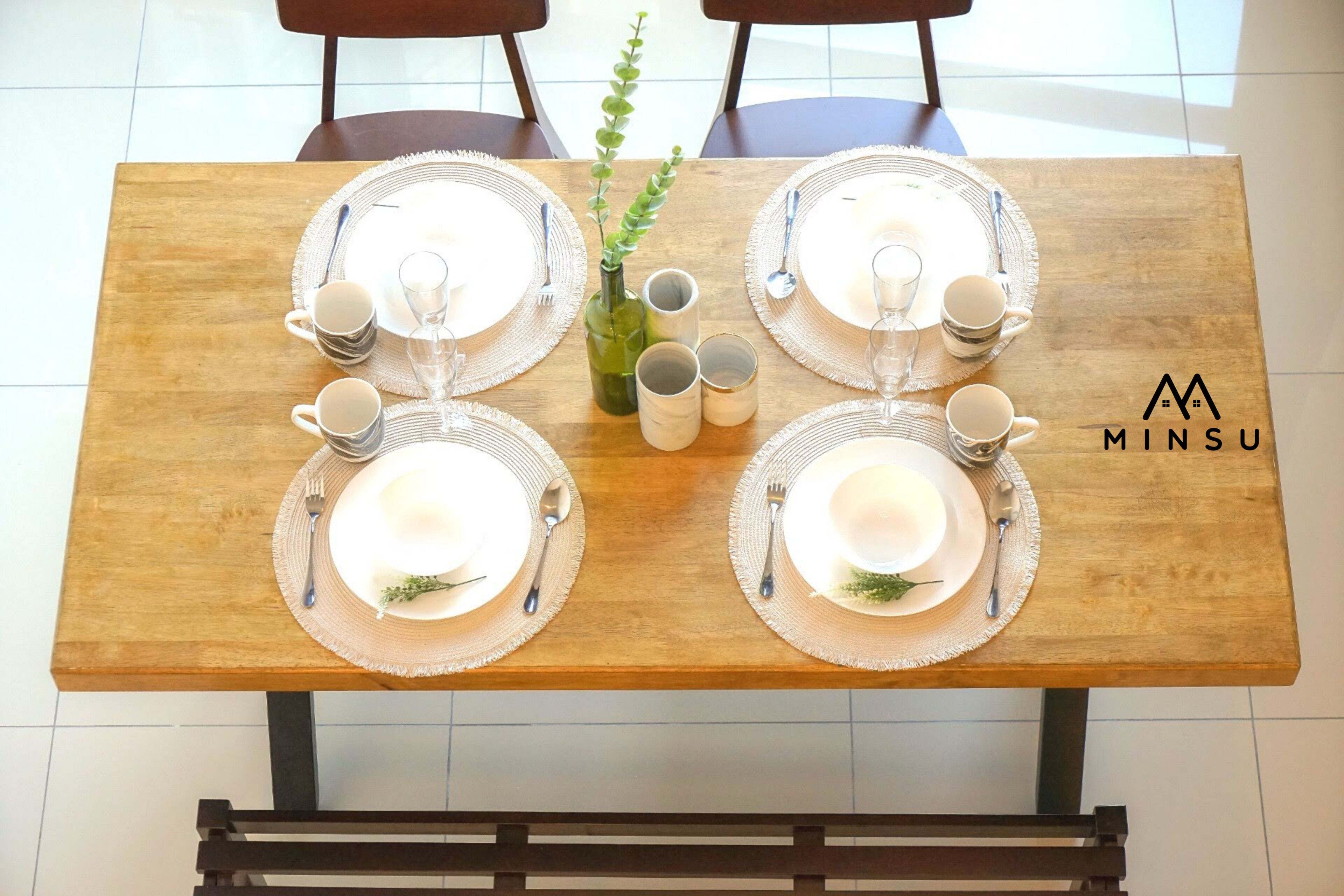 A wooden dining table set with plates, cutlery, and glasses, with a logo on the table.