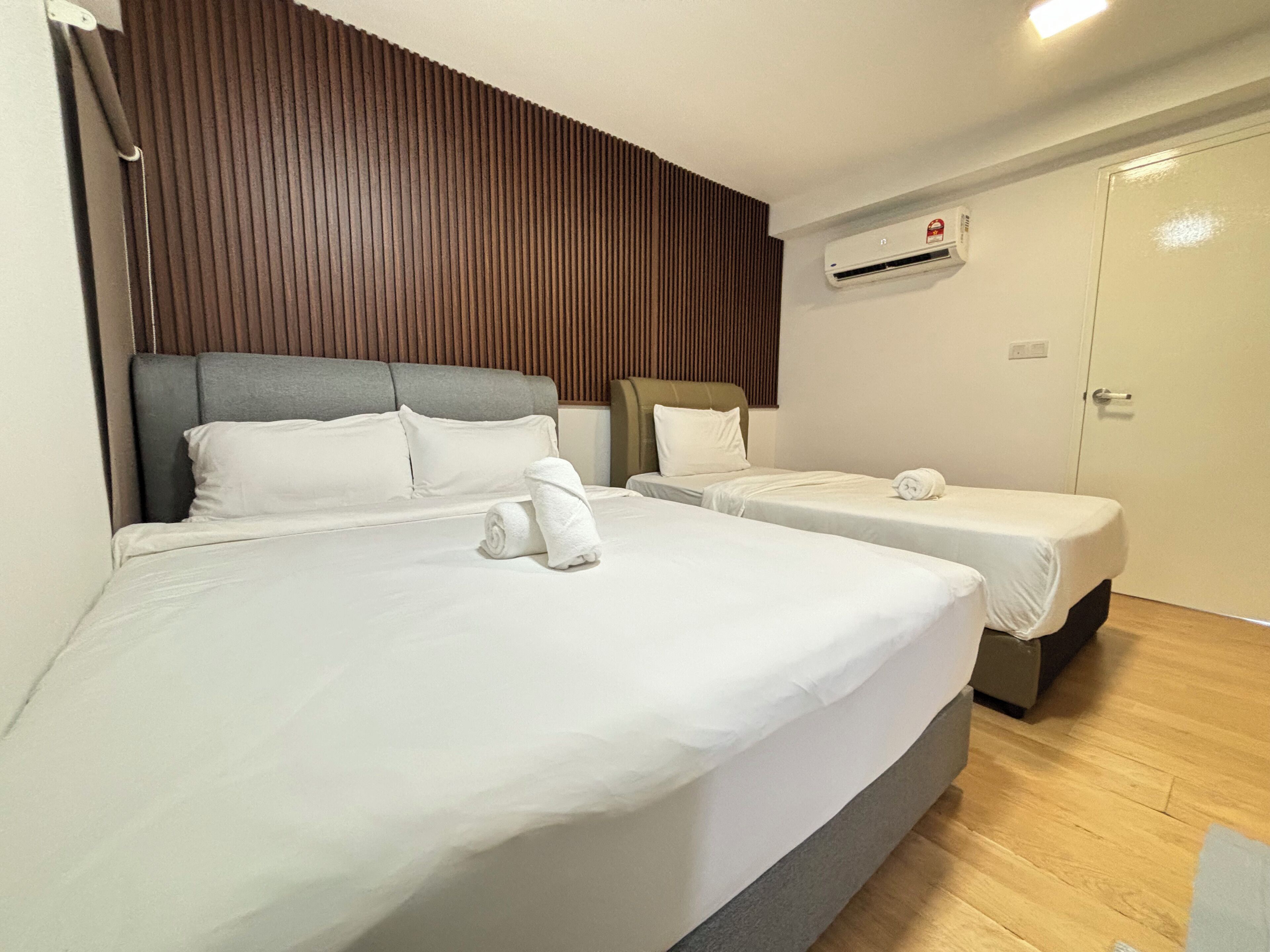 A hotel room with two beds, a wooden headboard, a wall-mounted air conditioner, and a door.