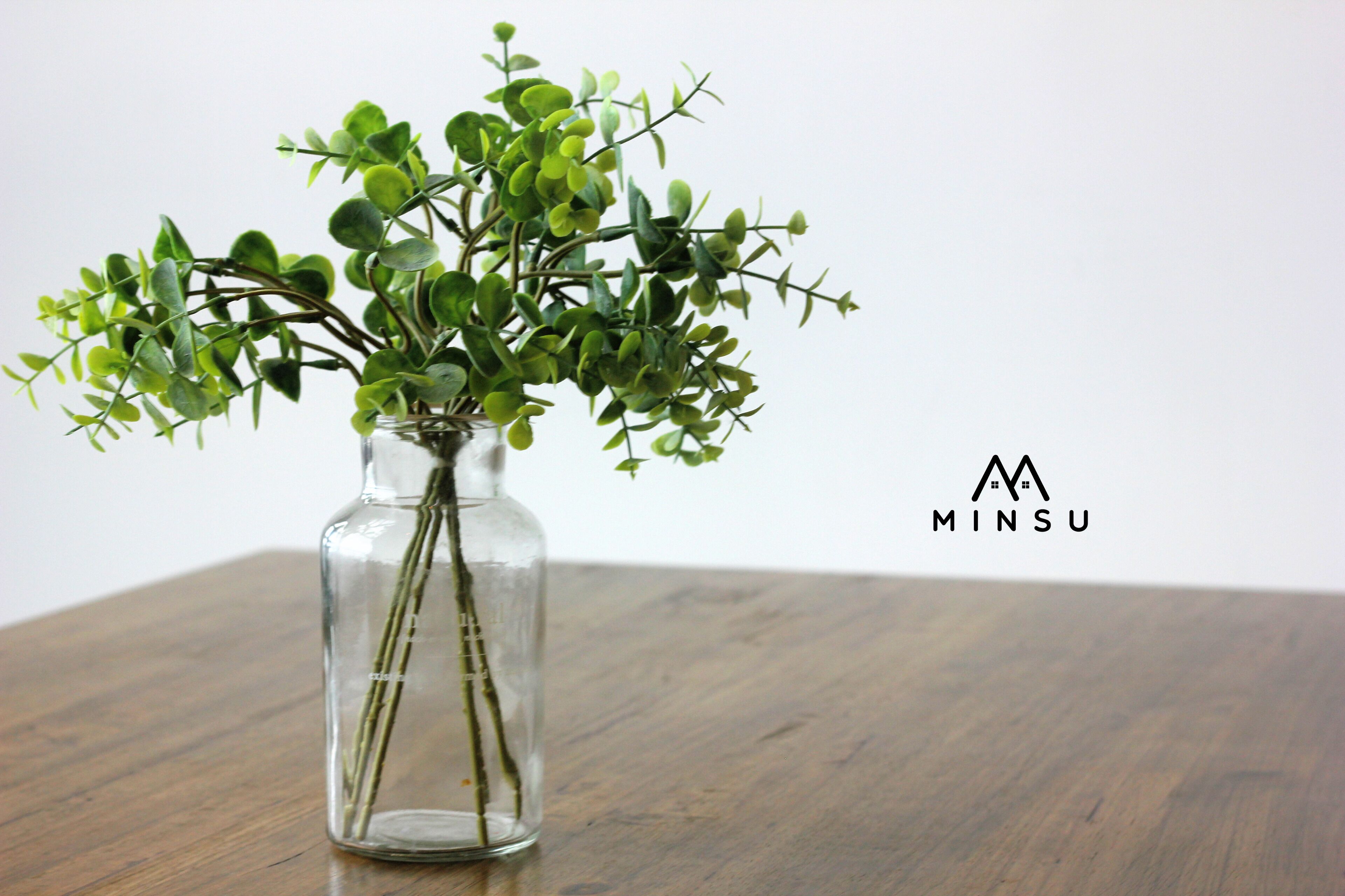 A clear glass vase with green foliage on a wooden table.