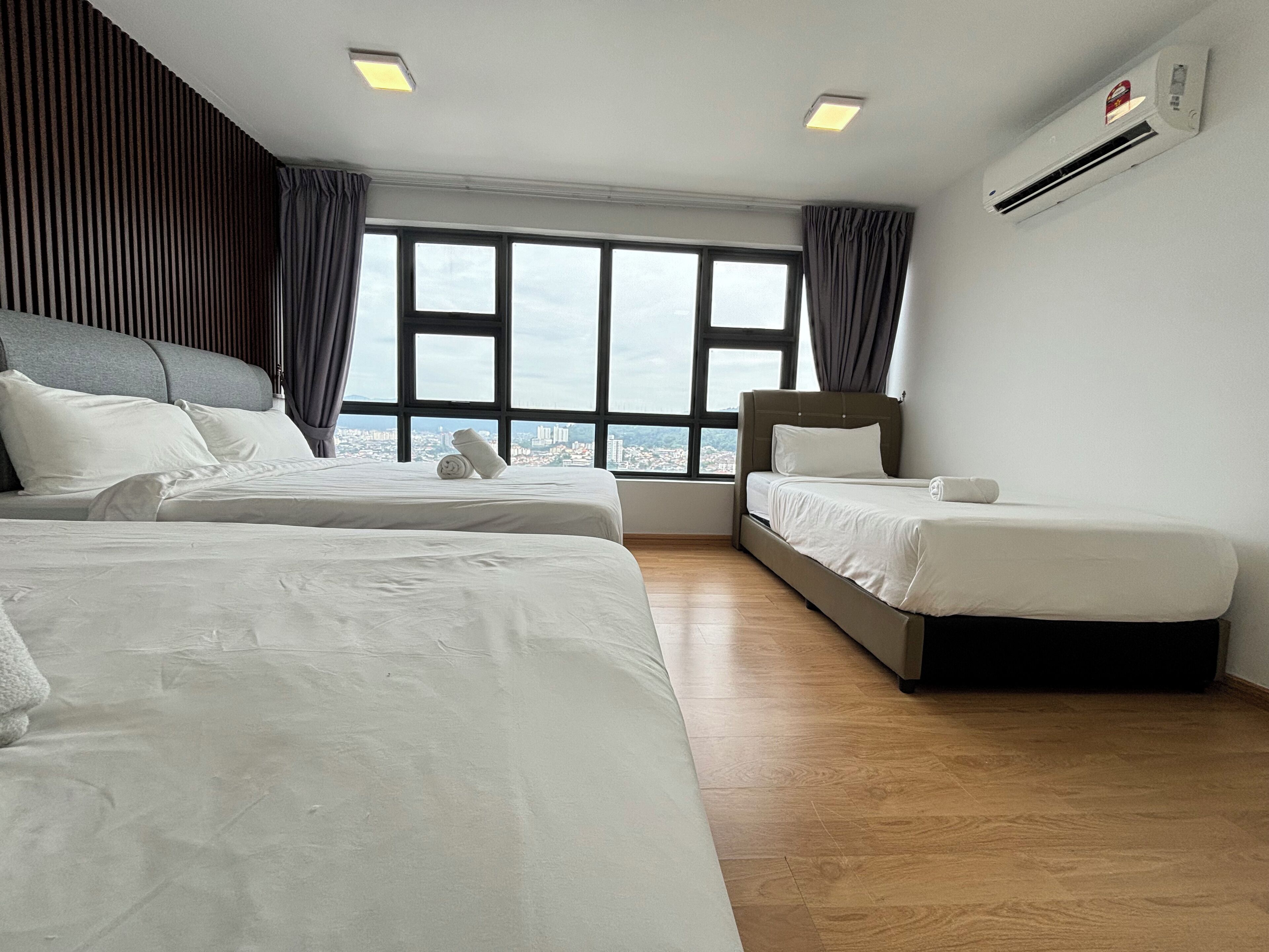 Ein Hotelzimmer mit zwei Betten, einem großen Fenster mit Blick auf die Stadt und einer Klimaanlage an der Wand.