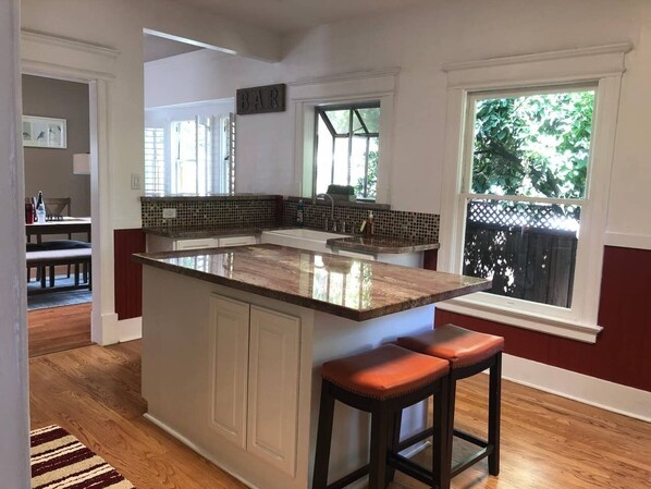 A kitchen with a large island, wooden bar stools, and a view of the outdoors through a window.