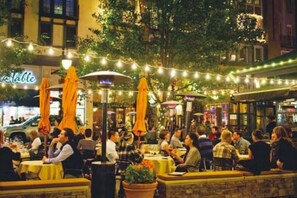 An outdoor dining area with tables and chairs, string lights, and umbrellas.
