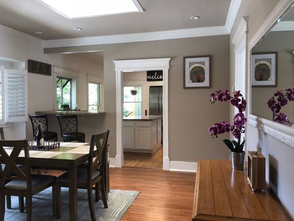Un comedor con una mesa y sillas de madera, una cocina al fondo, y un letrero que dice 'welcome'.