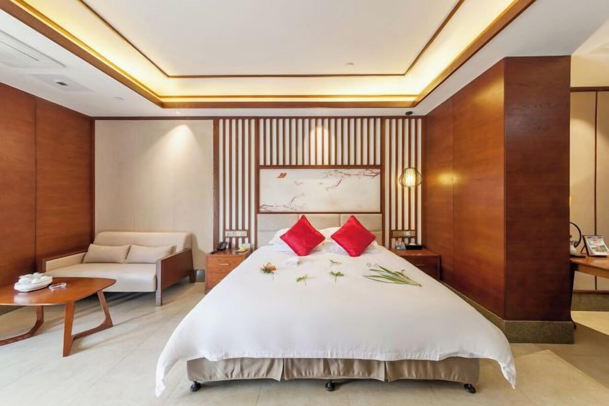 A hotel room with a large bed, a sofa, a bedside table, and a wall-mounted artwork.