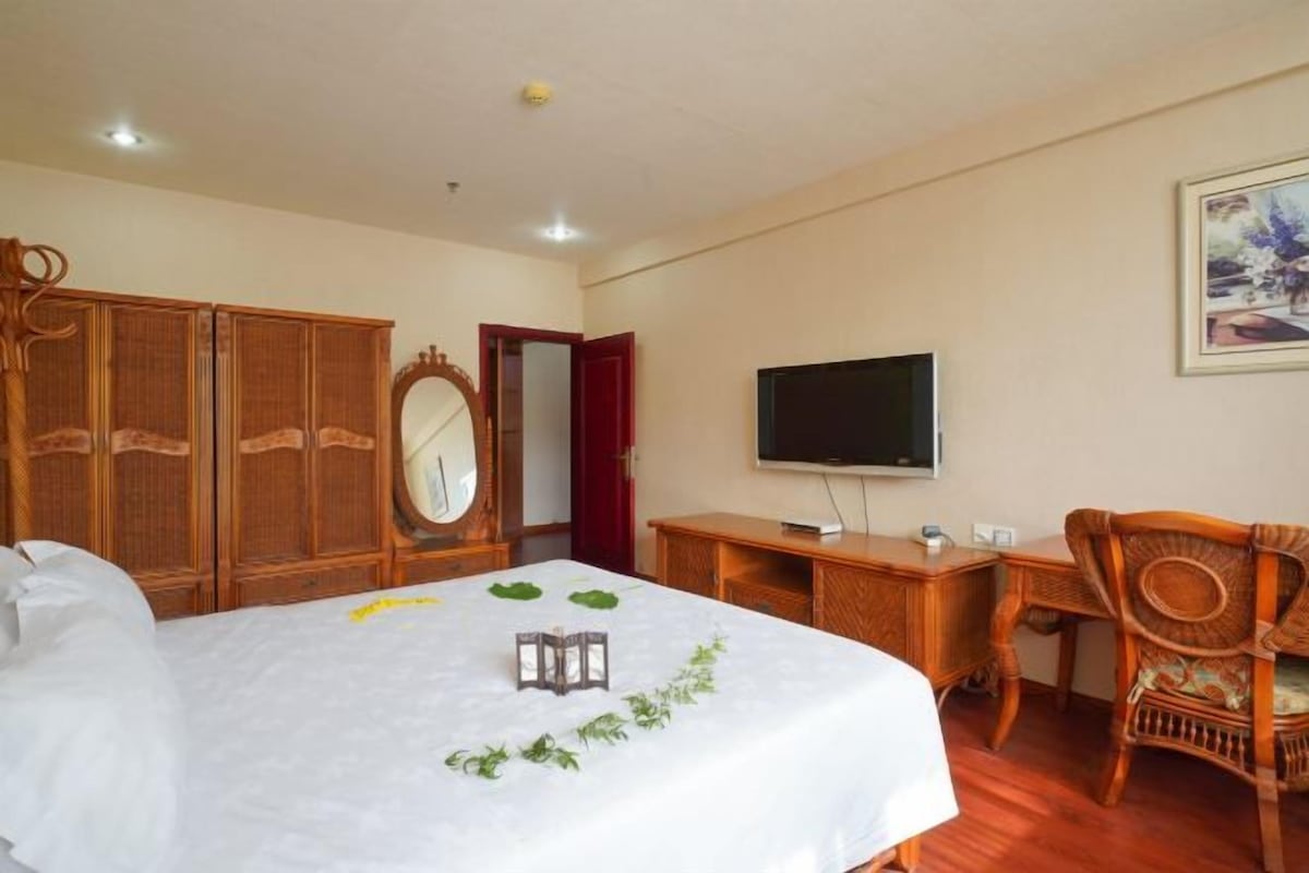 A hotel room with a bed, wooden wardrobe, a television, a desk, and a chair.