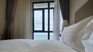 A hotel room with a large bed, a nightstand with a lamp, and a view of the sea through a window with curtains. - Timurbay by Seascape (Kuantan)