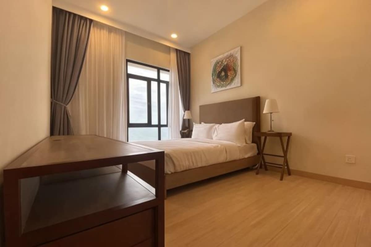 Una habitación de hotel con cama, mesita de noche, lámpara y ventana con cortinas.