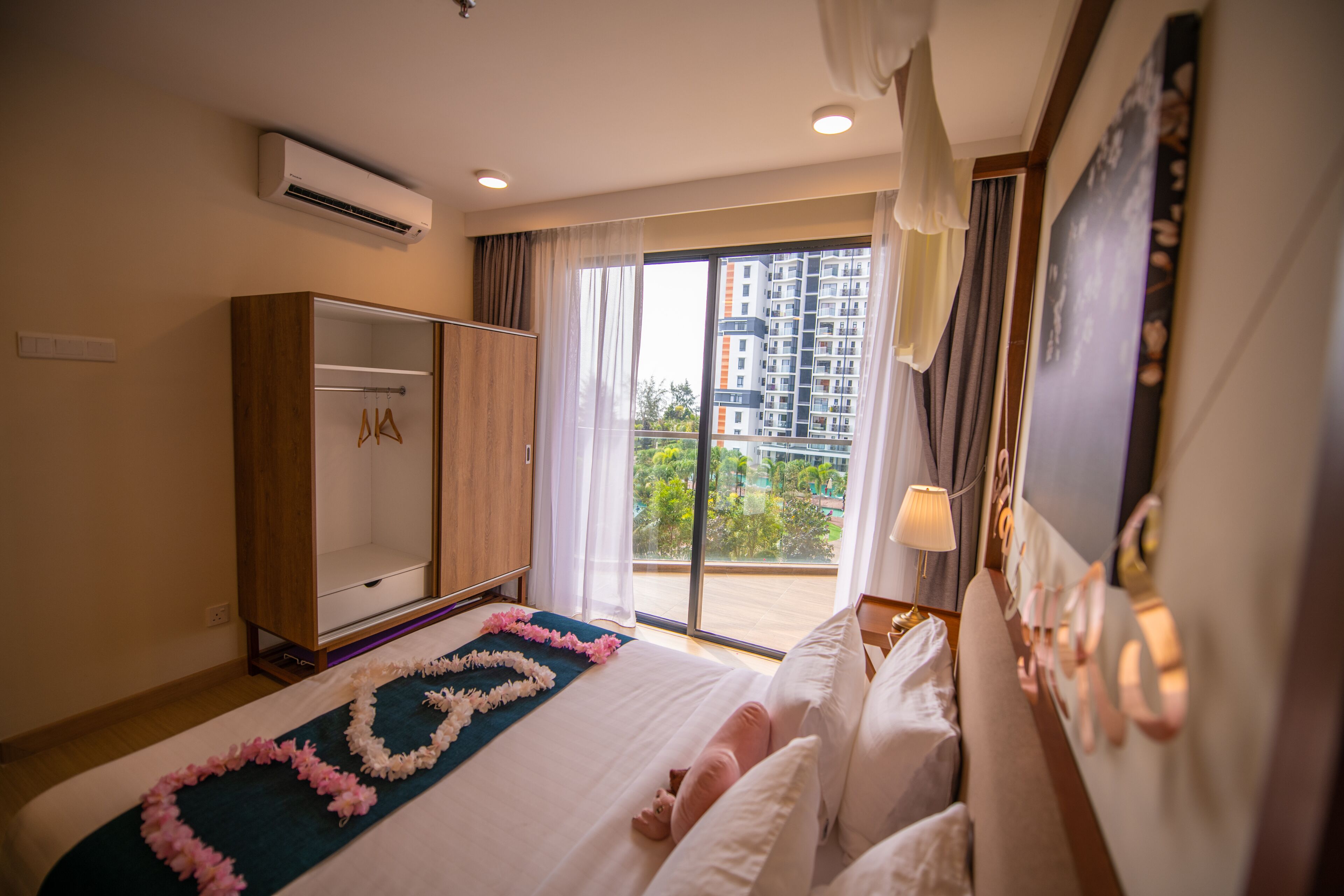 Quarto de hotel com cama, guarda-roupa, uma janela grande com vista para edifícios e um ar condicionado.