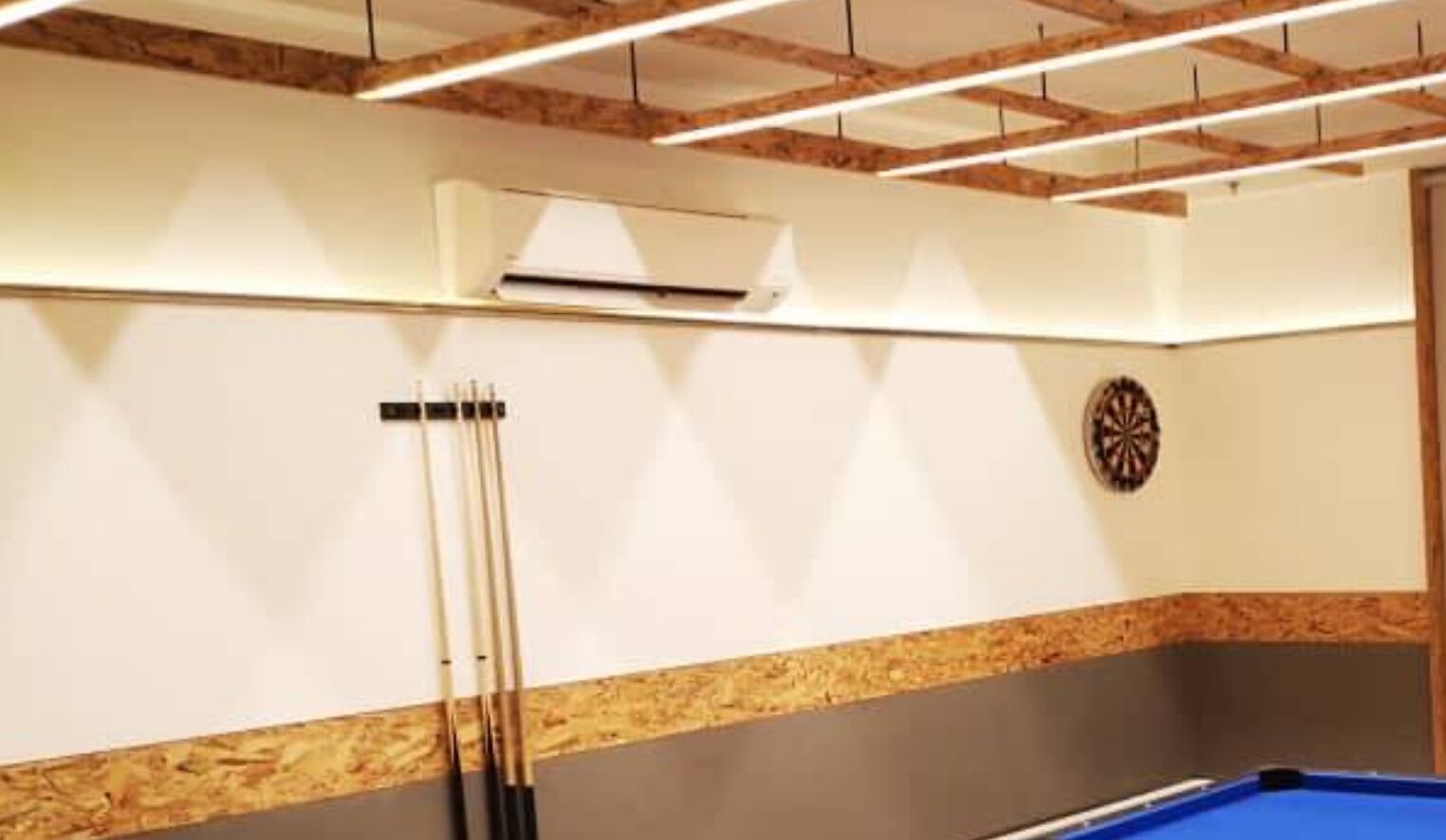 A billiards table with a dartboard and cue sticks in a room with wooden beams and a white wall.