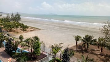 Vista de una playa desde un resort, con palmeras, una piscina y cielo despejado.