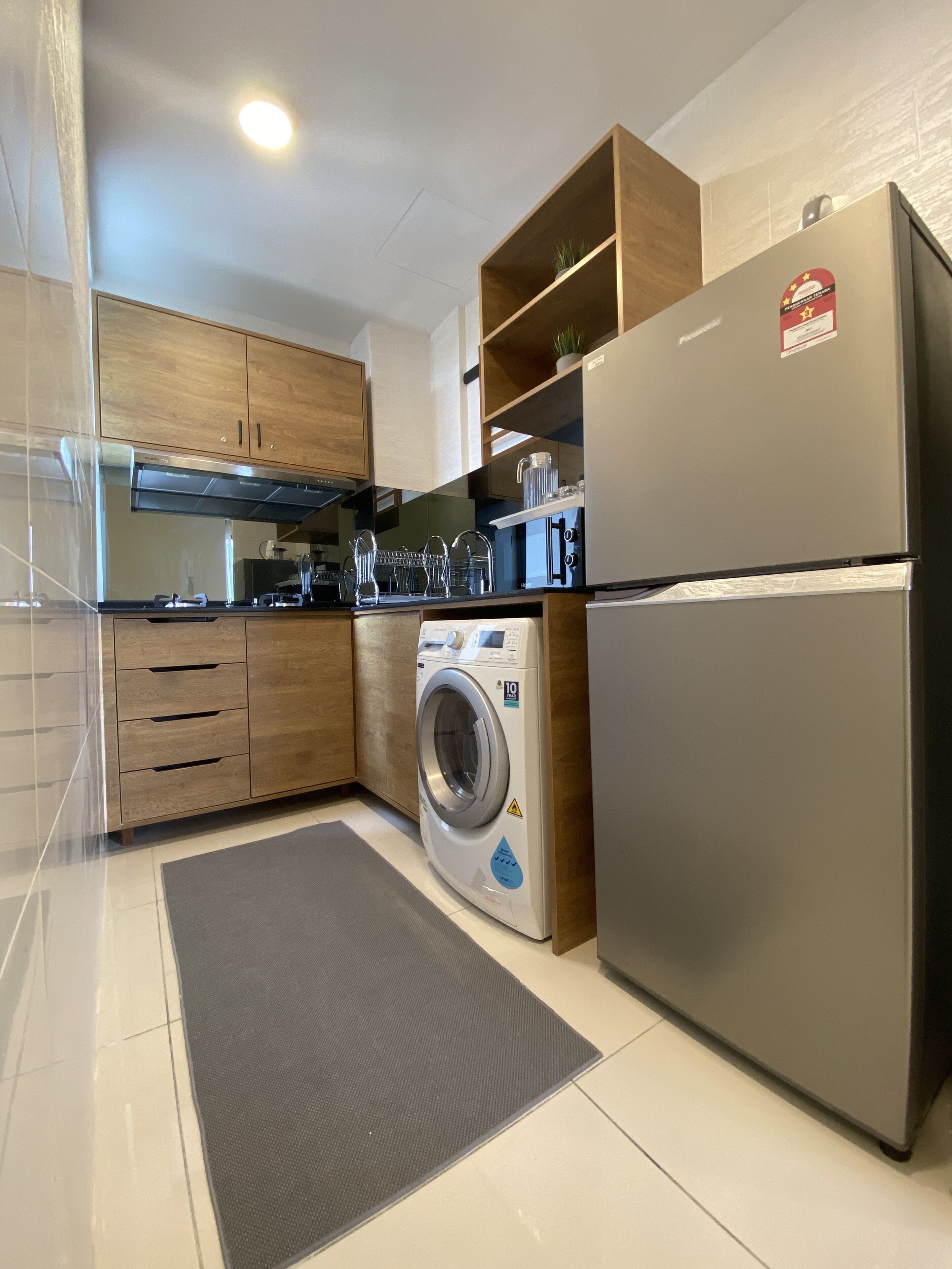 A modern kitchen with wooden cabinets, a stainless steel refrigerator, a washing machine, and a coffee maker.