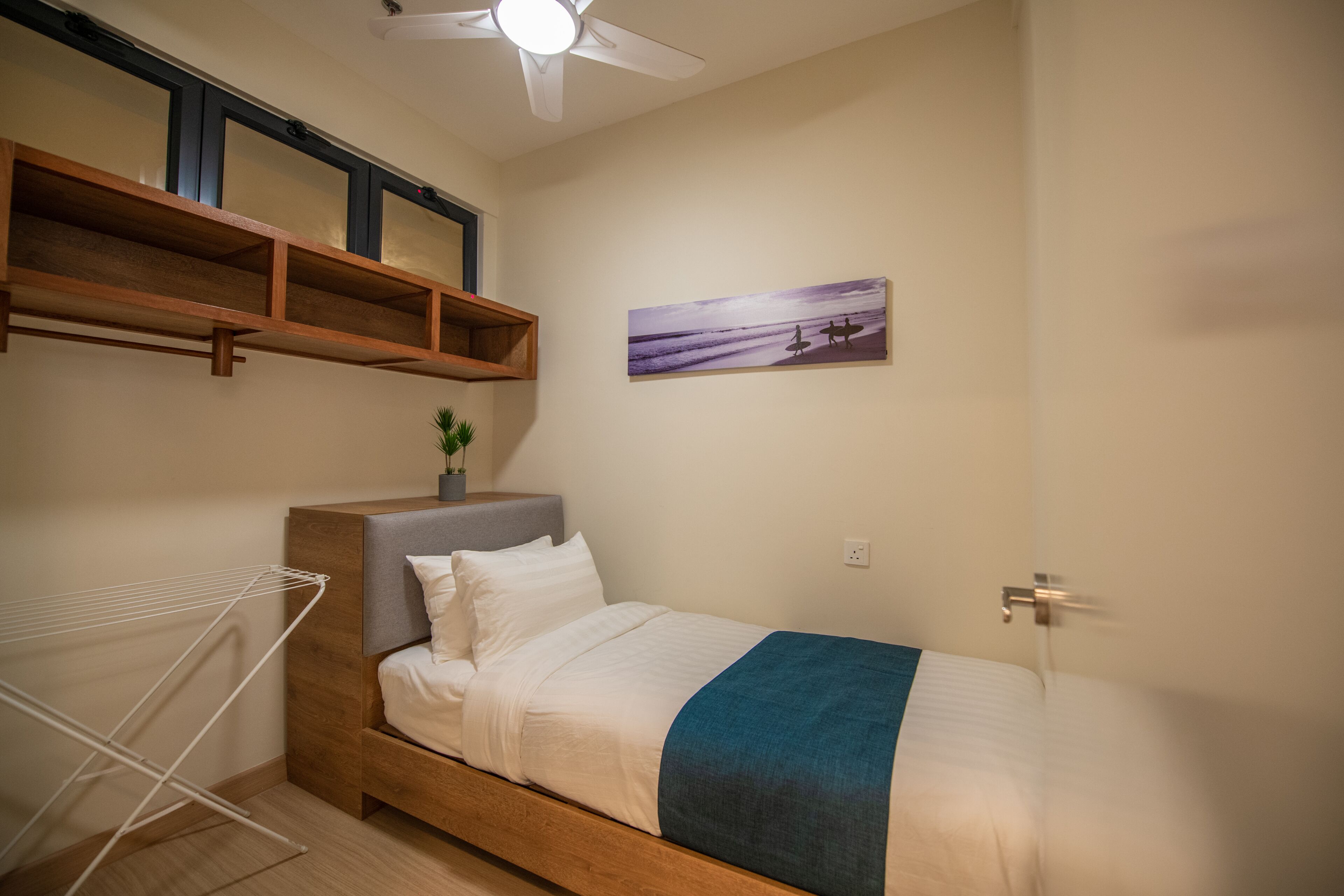 Quarto com cama, ventoinha no teto, prateleira na parede e um quadro.