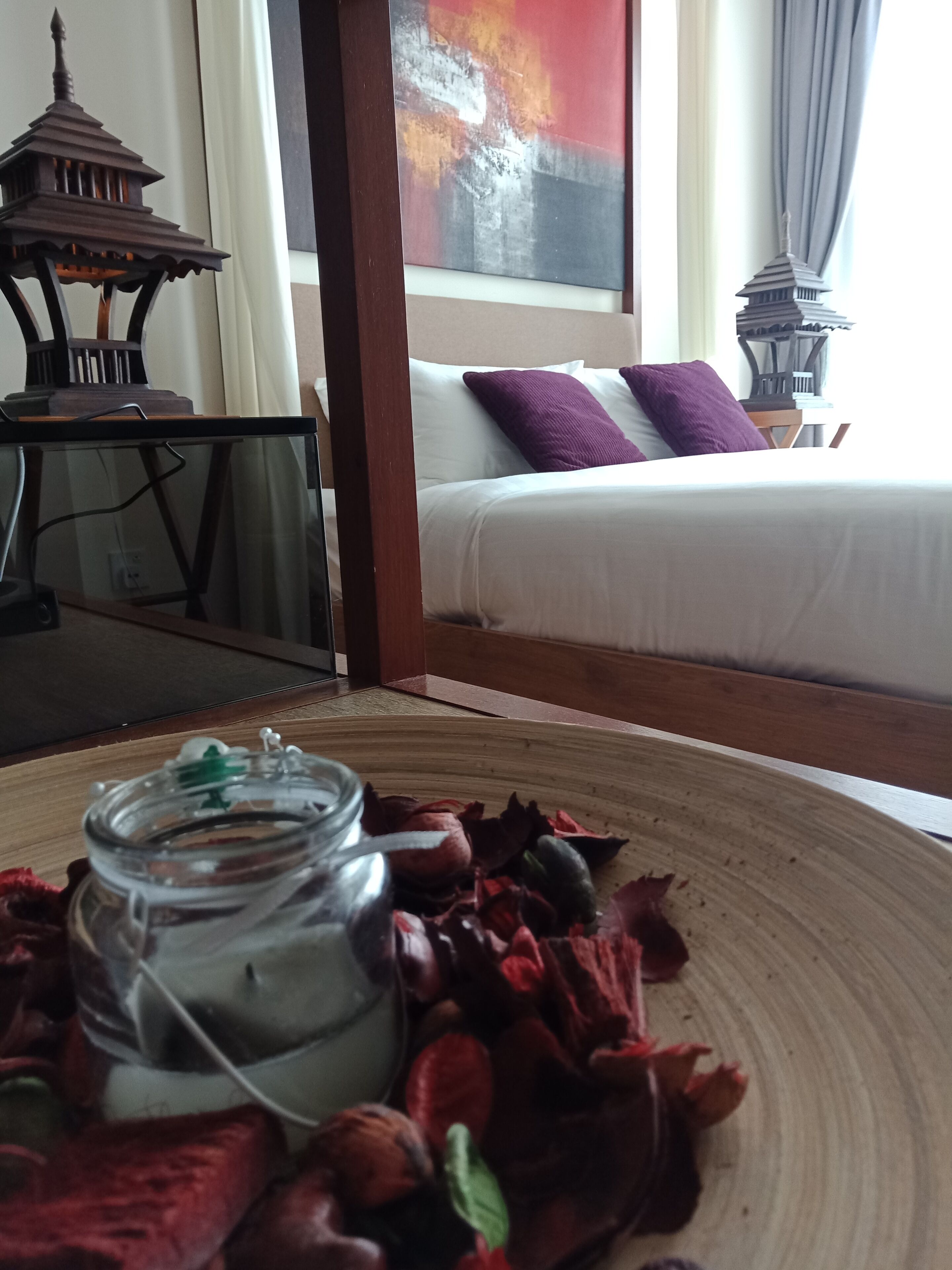 A room with a bed, a decorative lantern, and a glass jar with a green lid on a woven mat.