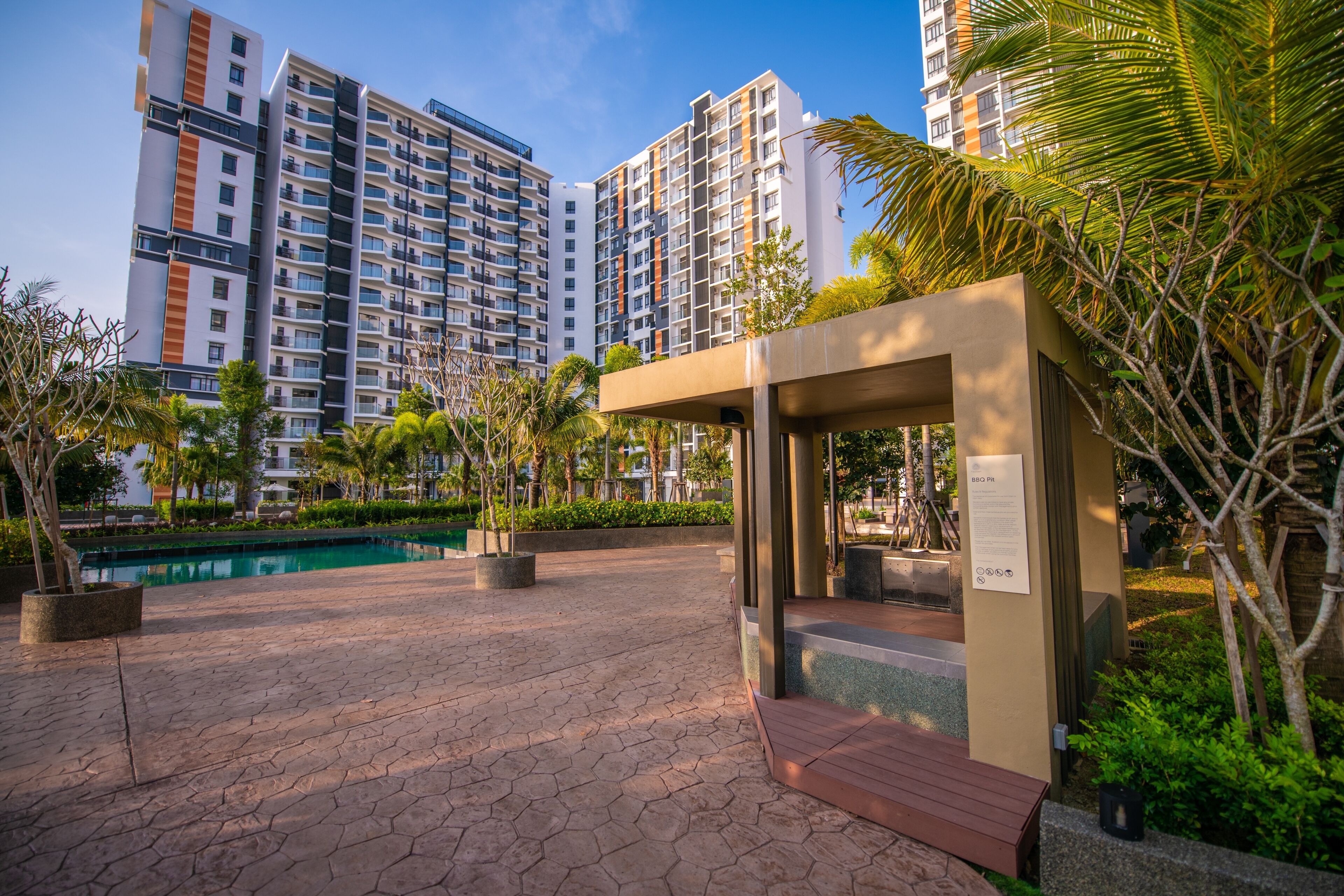 A modern residential complex with a swimming pool, landscaped areas, and high-rise buildings in the background.