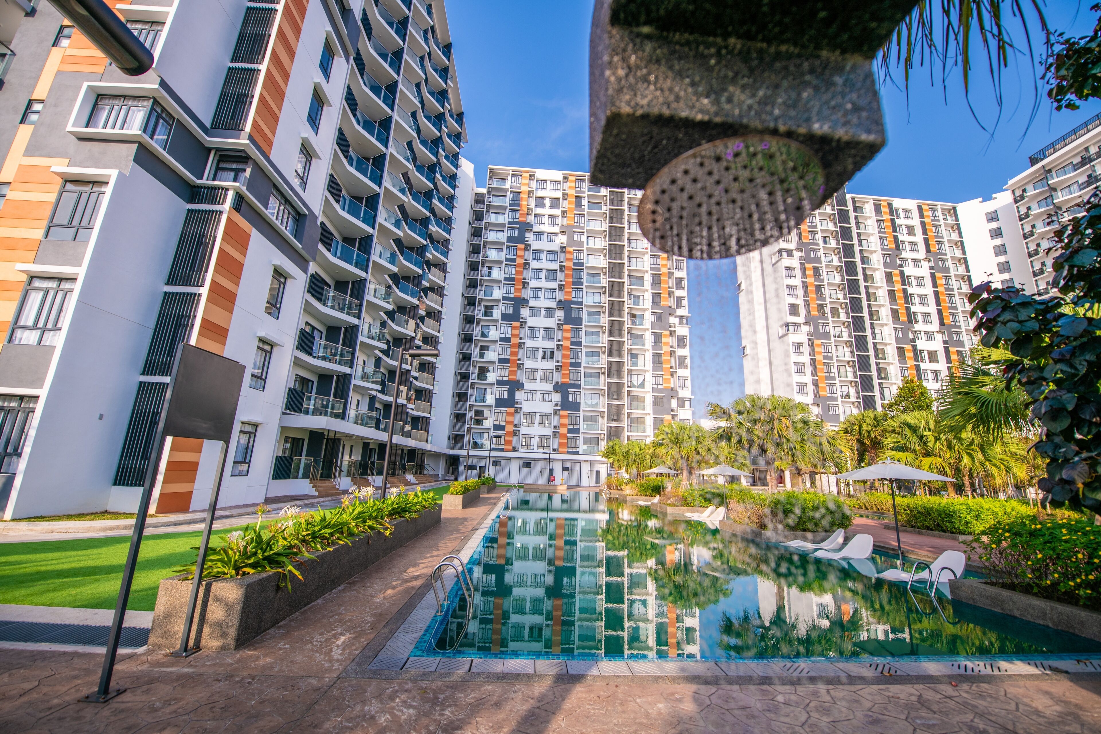 A modern residential building with a swimming pool, balconies, and lush greenery.