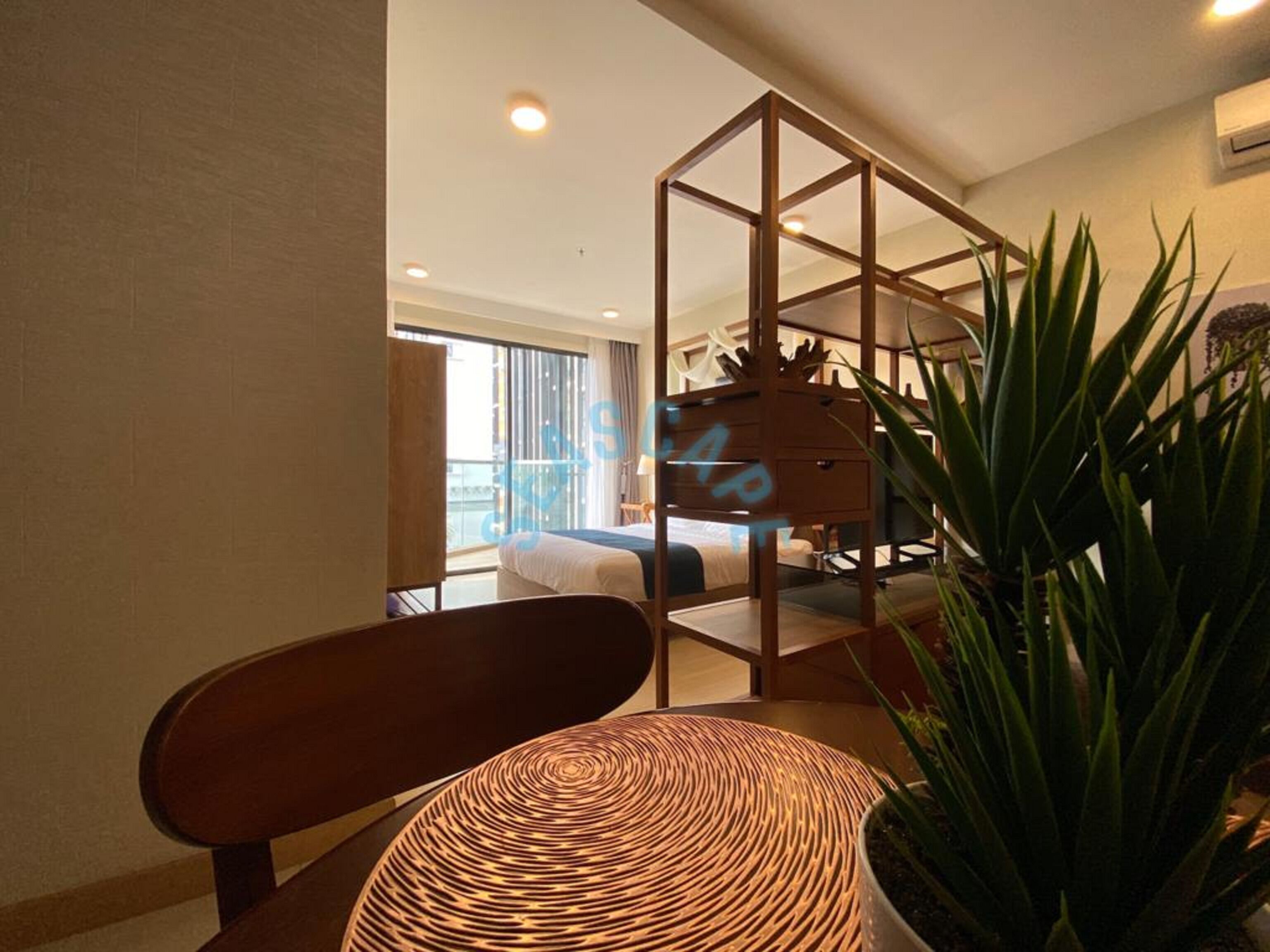 A hotel room with a bed, a wooden chair, a woven table, and a potted plant.
