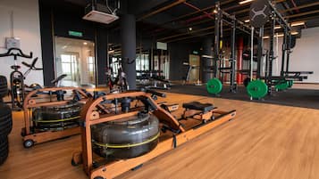 Un gimnasio con máquinas de remo, equipo de levantamiento de pesas y piso de madera.