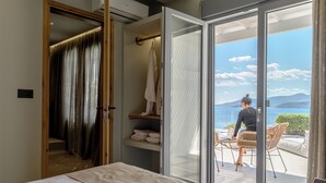 Ein Schlafzimmer mit Bett, Nachttisch, Fenster mit Meerblick und einer Schiebetür, die auf einen Balkon führt.