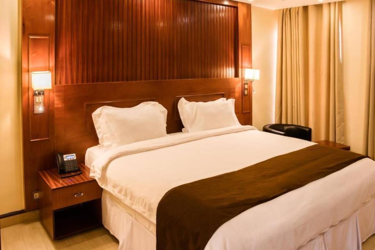 Une chambre d’hôtel avec une tête de lit en bois, un lit avec du linge de lit blanc, un téléphone sur la table de chevet et une petite table de nuit.