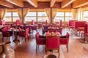 A restaurant with wooden floors, red upholstered chairs, and tables set with orange napkins. - Sainte Famille Hotel (Kigali)