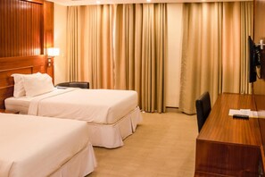 A hotel room with two beds, a desk, a chair, and a TV. - Sainte Famille Hotel (Kigali)
