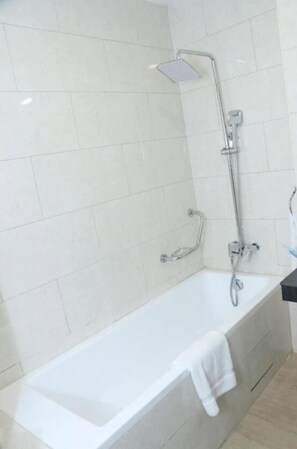 Un baño con una bañera blanca, un cabezal de ducha y una toalla colgada en la pared.