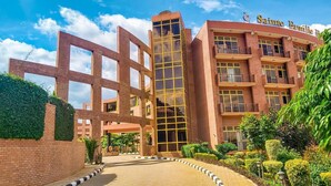 A multi-story building with a prominent entrance featuring a geometric metal gate. The building has a brick facade with large windows and balconies. - Sainte Famille Hotel (Kigali)