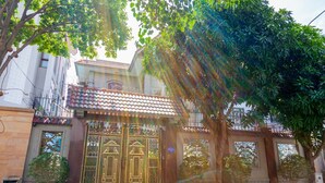 A building with a traditional tiled roof, a gated entrance, and a small garden area with trees and shrubs. - Villa Binh Minh (Ho Chi Minh City)