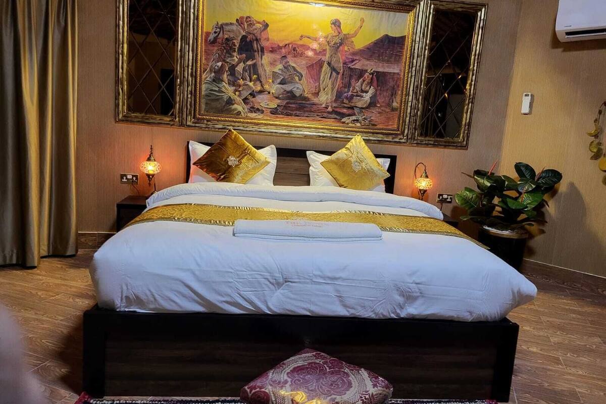 Ein Hotelzimmer mit einem großen Bett, zwei Nachttischen, einer Stehlampe und einem gerahmten Bild sowie einer Zimmerpflanze.
