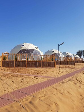 Une rangée de tentes en forme de dôme, séparées par une clôture en bois, dans un paysage désertique.
