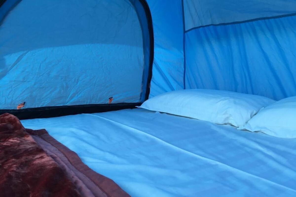 Ein Zelt mit einem Bett, inklusive Moskitonetz und weißer Bettwäsche.