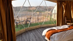 Un dormitorio con un ventanal grande, una cama y vistas a un área cercada con sillas afuera.