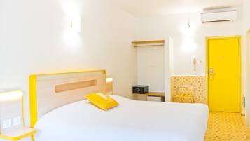 Een hotelkamer met een bed, nachtkastje, lamp en een gele deur.