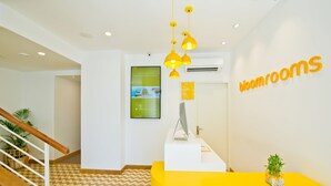 A reception area with a yellow desk, a computer, and a plant. There is a staircase with a wooden handrail and a patterned floor. - Bloomrooms @ City Centre (Bengaluru)