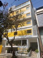 Ein mehrstöckiges Gebäude mit einer gelb-weißen Fassade, einem Schild mit der Aufschrift "Bloomrooms" und einer Treppe, die zum Eingang führt.