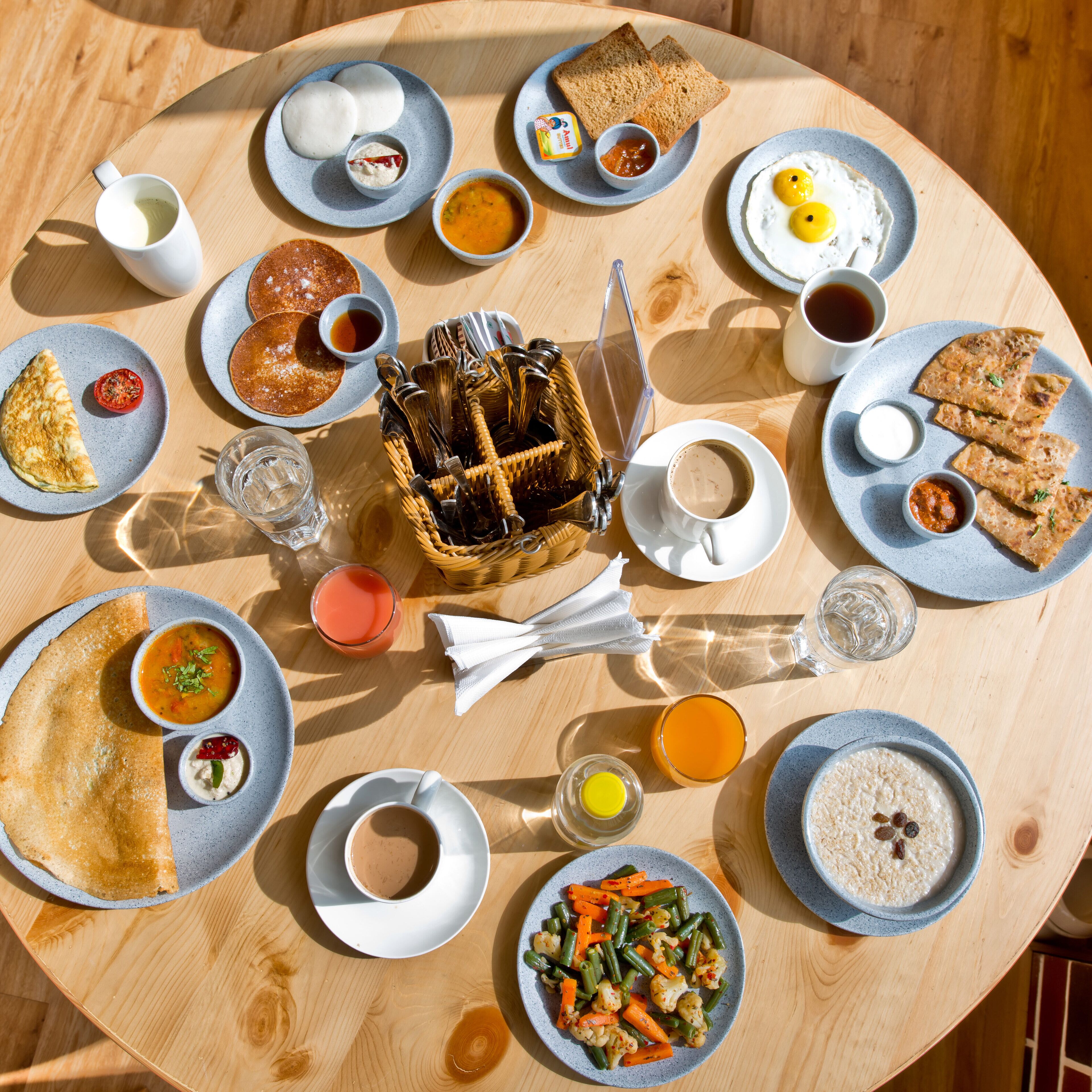 A round wooden table with various breakfast items including toast, eggs, pancakes, and a fruit salad.