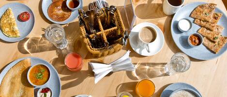 Una mesa redonda de madera con diversos alimentos para el desayuno, incluyendo tostadas, huevos, tortitas y una ensalada de frutas.
