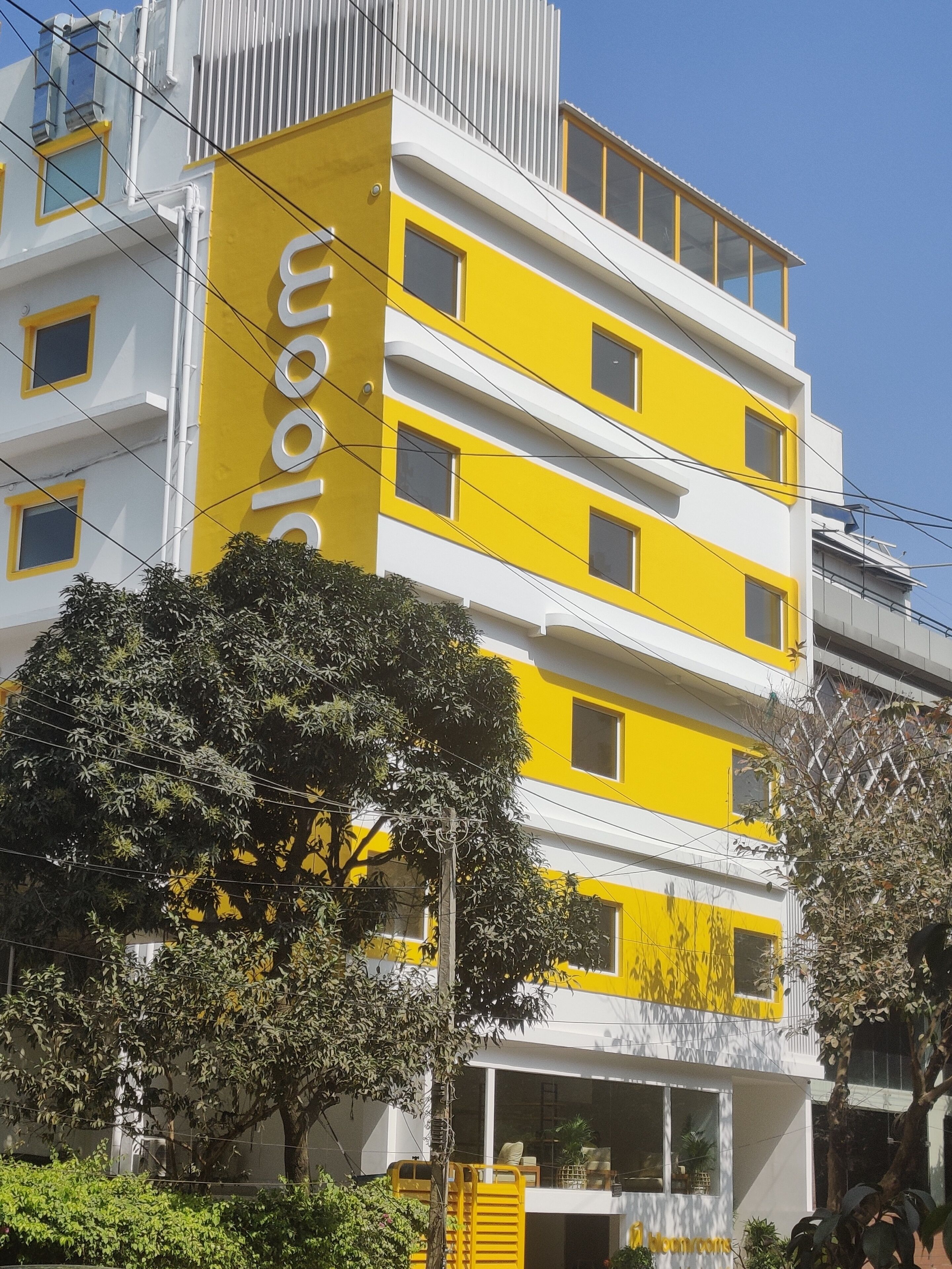 Un edificio de varios pisos con fachada amarilla y blanca, ventanas grandes y un balcón visible.