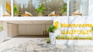 A modern building with a large glass facade, a sign reading "bloomrooms," and a small garden area with potted plants. - Bloomrooms @ City Centre (Bengaluru)