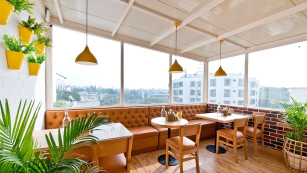 A modern interior with a wooden table and chairs, a round table with a bottle and a glass, and a bench seating area. - Bloomrooms @ City Centre (Bengaluru)