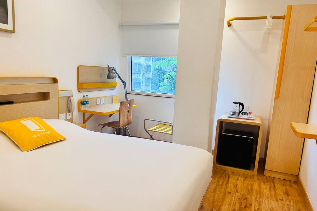 A hotel room with a bed, a desk, a chair, a small cabinet, and a window.