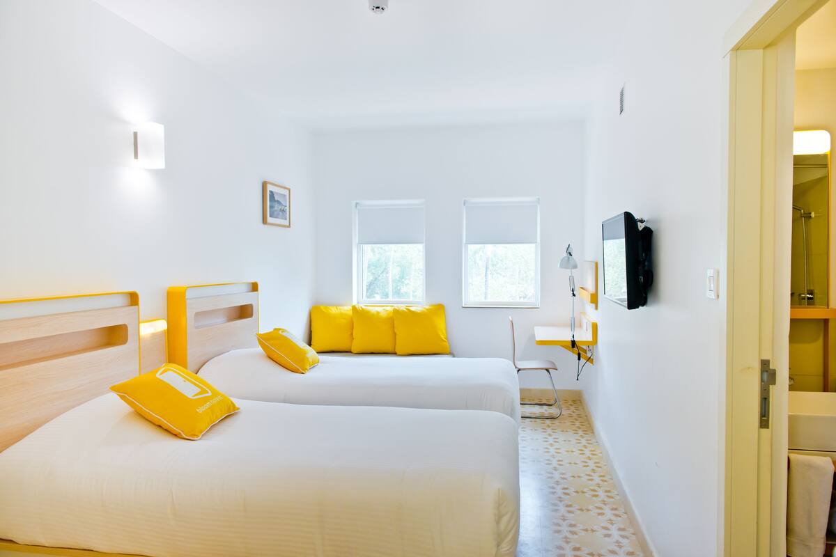 A hotel room with two beds, a desk, a chair, a TV, and a bathroom visible through an open door.