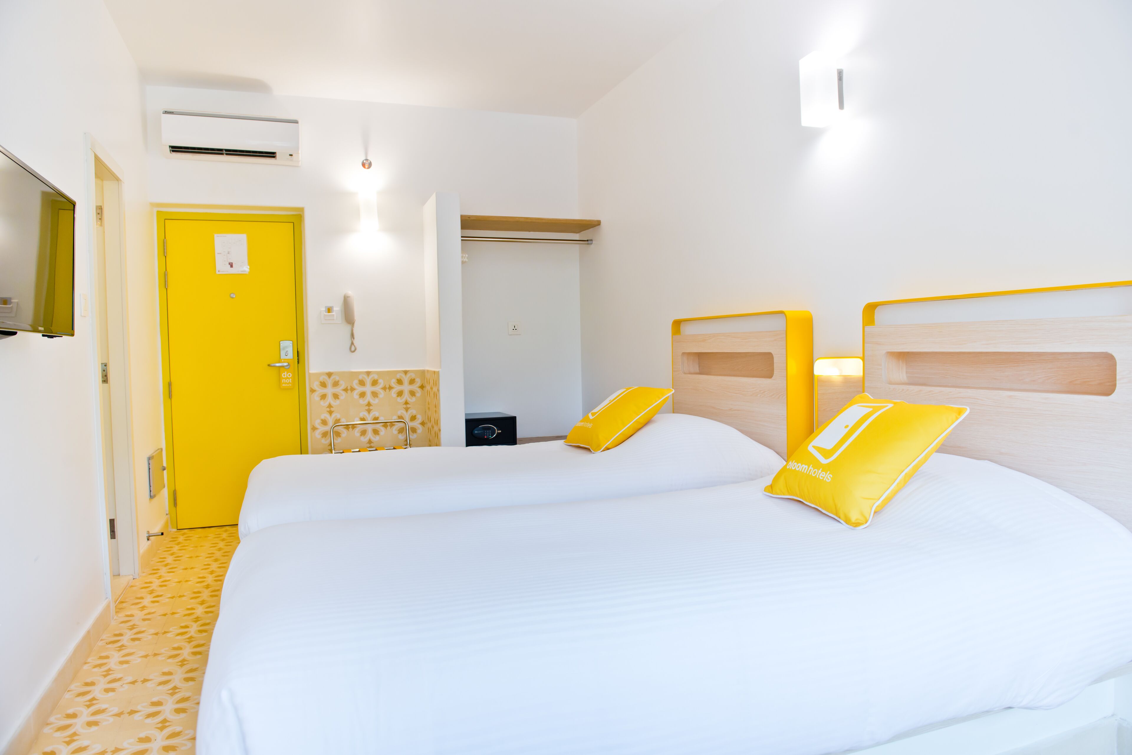 A hotel room with two beds, a yellow door, a mirror, and a small bedside table.