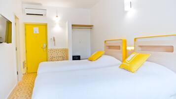 A hotel room with two beds, a yellow door, a mirror, and a small bedside table.