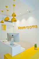 A reception desk with a computer, a small plant, and a sign reading "bloomrooms".